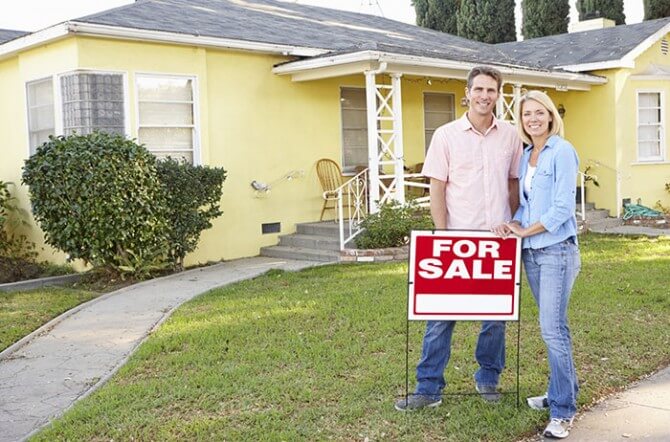 couple in front of "for sale" sign and house