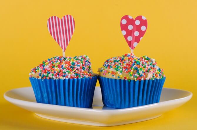 Bright and cheery red blue and yellow theme cupcakes with hundred and thousands candy topping and heart toppes for birthday or special occasion on yellow background.