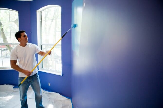 Young man painting wall with paint roller in house