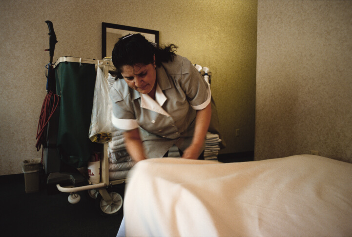 a hispanic woman at a hotel room tucks bedsheets into a bed