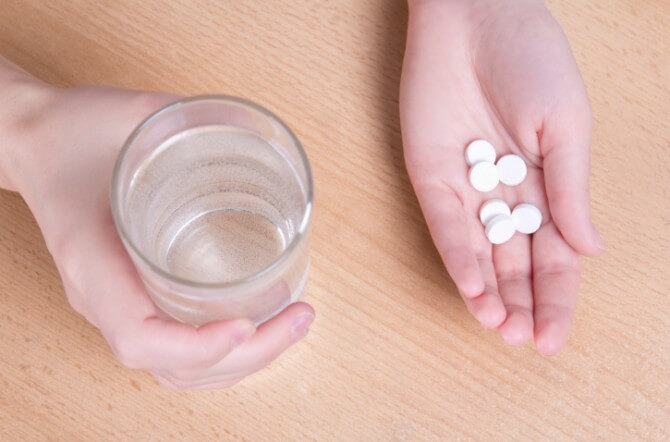 female hands with glass of water and pills