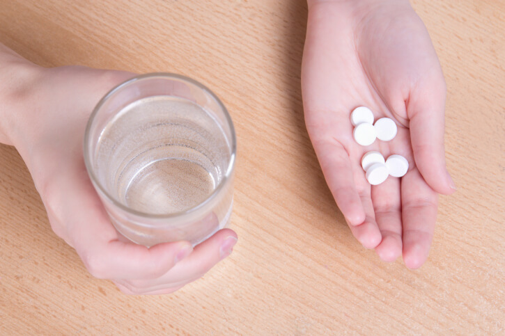 female hands with glass of water and pills